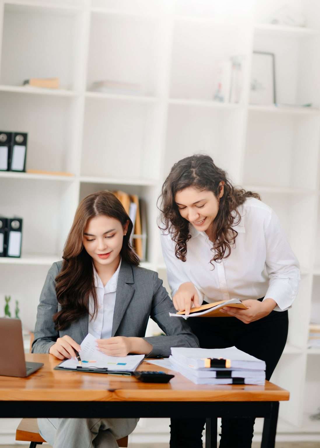Two businesswomen reviewing financial documents at an office desk, representing bookkeeping services by Peace of Mind Business Solutions.