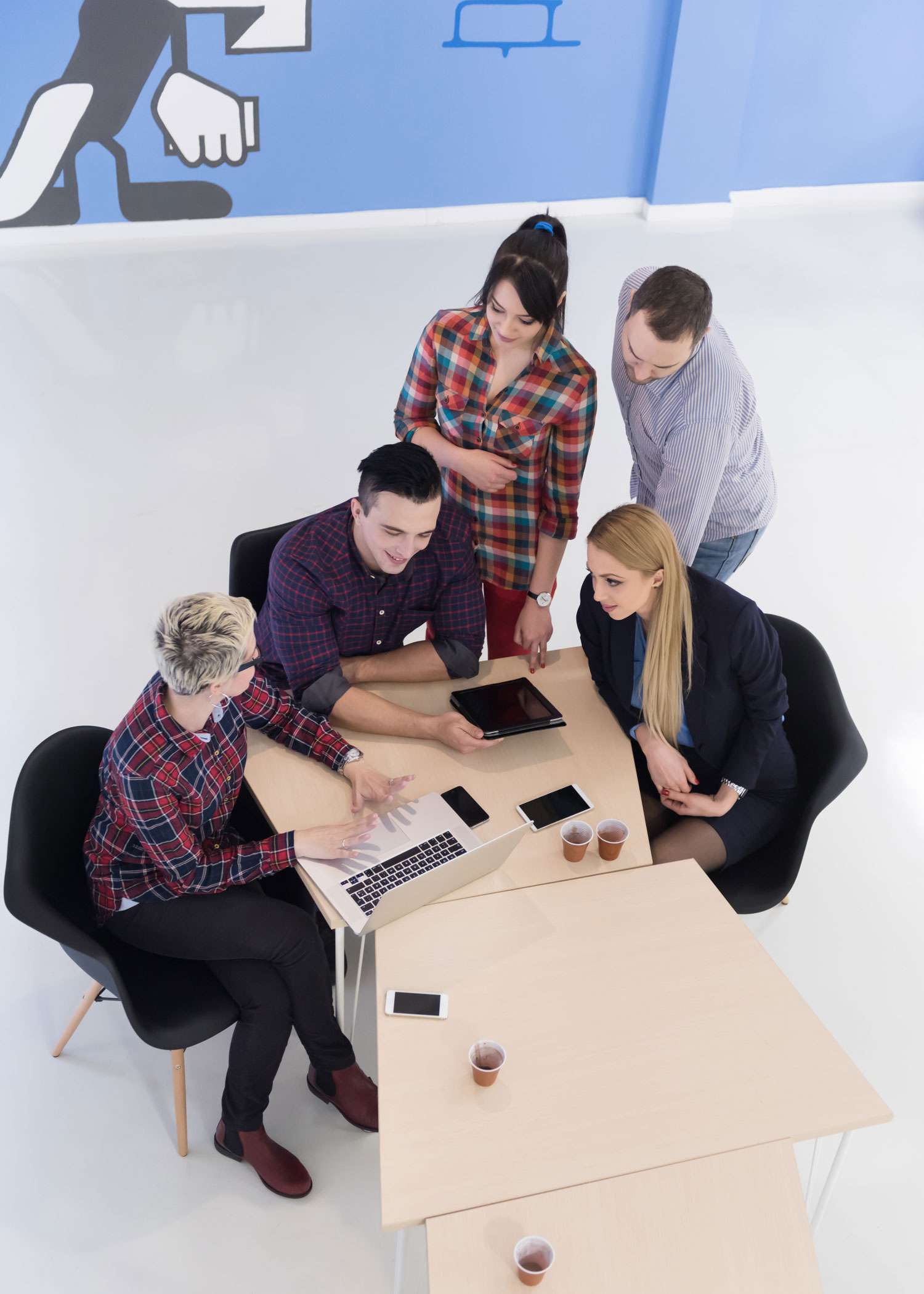 A diverse team of professionals collaborating around a table, working on laptops and tablets, illustrating efficient and coordinated payroll services by Peace of Mind Business Solutions.