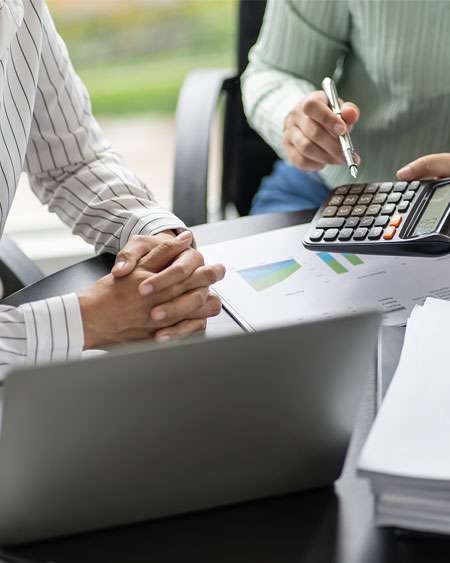 Two business professionals working at a desk, one using a calculator and the other reviewing documents, symbolizing payroll support services.