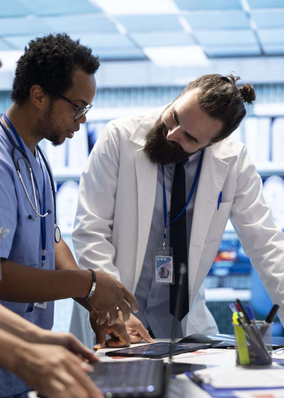Two healthcare professionals collaborate at a workstation, reviewing information on a tablet in a modern medical setting.